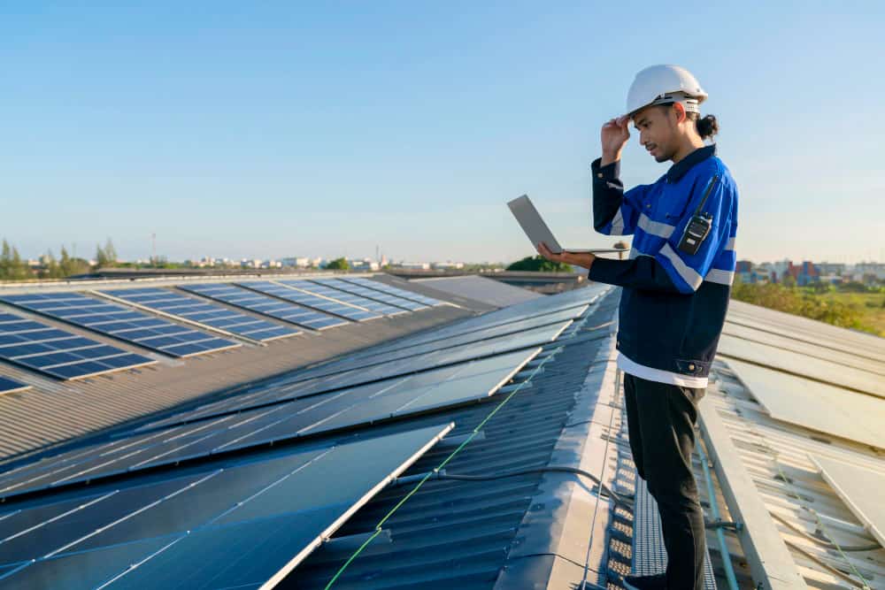 un technicien qui tient un ordinateur portable debout sur une toiture photovoltaïque industrielle