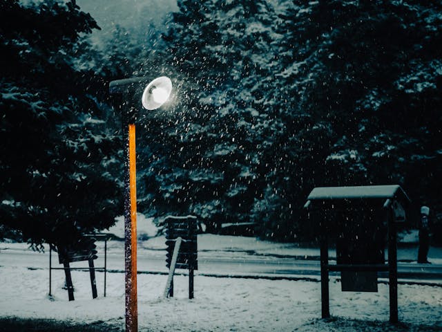 un lampadaire allumé avec de la neige aoutour, éclairage public solaire commune